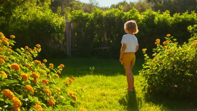 Niño alcanza flores en un jardín soleado